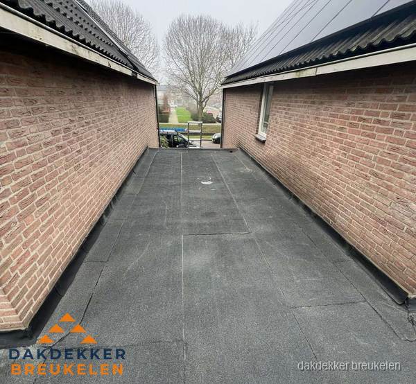 Plat dak met bitumen dakbedekking tussen bakstenen muren in Breukelen
