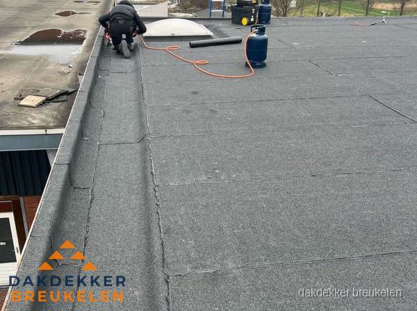 Dakdekker repareert bitumen dakbedekking op groot plat dak in Breukelen